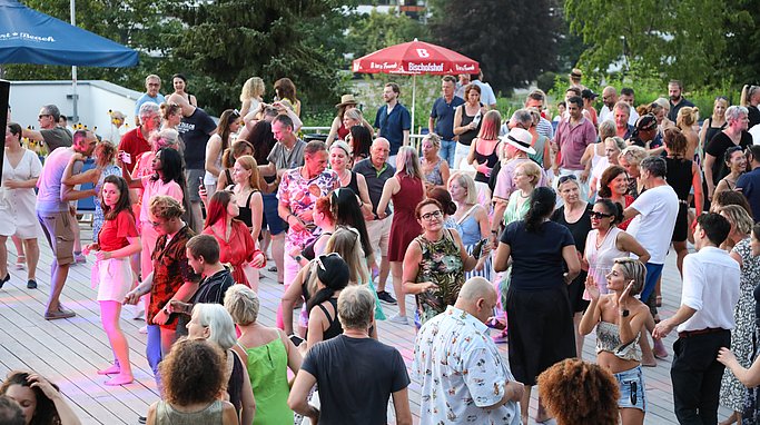 Die Diashow zeigt Eindrücke vom Salsa-Abend am Eckert Beach. Zu sehen sind tanzende Paare, Besucherinnen und Besucher im Publikum sowie die stimmungsvolle Atmosphäre der Veranstaltung am Abend.